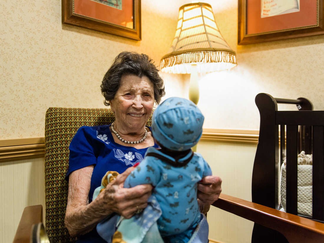 An older woman smiles while holding a Sundae companion doll